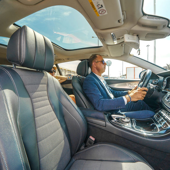 Professional taxi driver driving luxury car with passenger in back seat, modern interior and sunlight through panoramic roof

