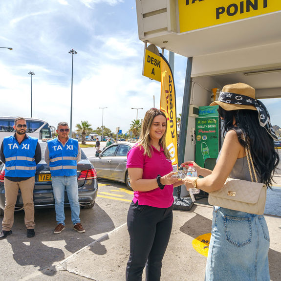 Taxi staff offers bottled water and welcome treats to arriving passenger at Heraklion Airport meeting point
